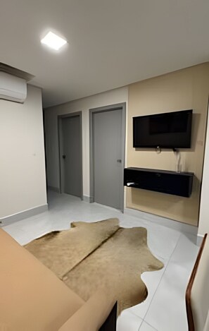 A modern bedroom with a flat-screen TV mounted on the wall, a large window, and a neutral color palette.