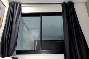 A room with a large window, black curtains, and a visible door leading to another room.