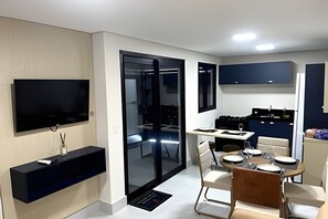 A modern kitchen with a dining area, a flat-screen TV, and a sliding glass door leading to a balcony.