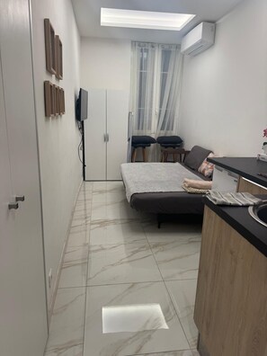 A compact room with a bed, a small kitchenette, a TV, and a window with sheer curtains. - Nice Old Town Studio, Sleeps 2 (Nice)