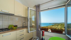 Une cuisine avec vue sur la mer, une fenêtre avec des rideaux et une table avec des verres à vin et une bouteille.