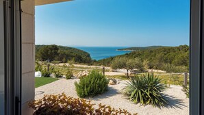 Un balcon offrant une vue sur un paysage côtier, comprenant des arbres, une étendue d’eau et une ligne de côte lointaine.