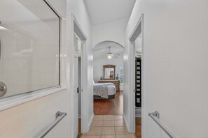 A narrow hallway with white walls, a ceiling fan, a bed with a checkered blanket, and a dresser with a mirror. - Poolside Heaven in Cumbrian Lakes (Kissimmee)