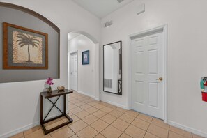 A hallway with a framed picture, a console table with a vase, a mirror, and a white door. - Poolside Heaven in Cumbrian Lakes (Kissimmee)