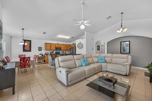 A modern living room with a sectional sofa, a dining area, and a kitchen in the background. - Poolside Heaven in Cumbrian Lakes (Kissimmee)