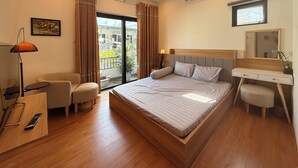 Ein Hotelzimmer mit Bett, Schreibtisch, Stuhl, Lampe, einem Fenster mit Vorhängen, einer Klimaanlage und einer kleinen Topfpflanze.