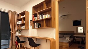 Ein modernes Zimmer mit einem Holztisch, zwei schwarzen Stühlen, einem Bücherregal und einem Bett.
