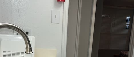 A kitchen with a stainless steel sink, a white countertop, a white wall, and a red fire extinguisher mounted on the wall.