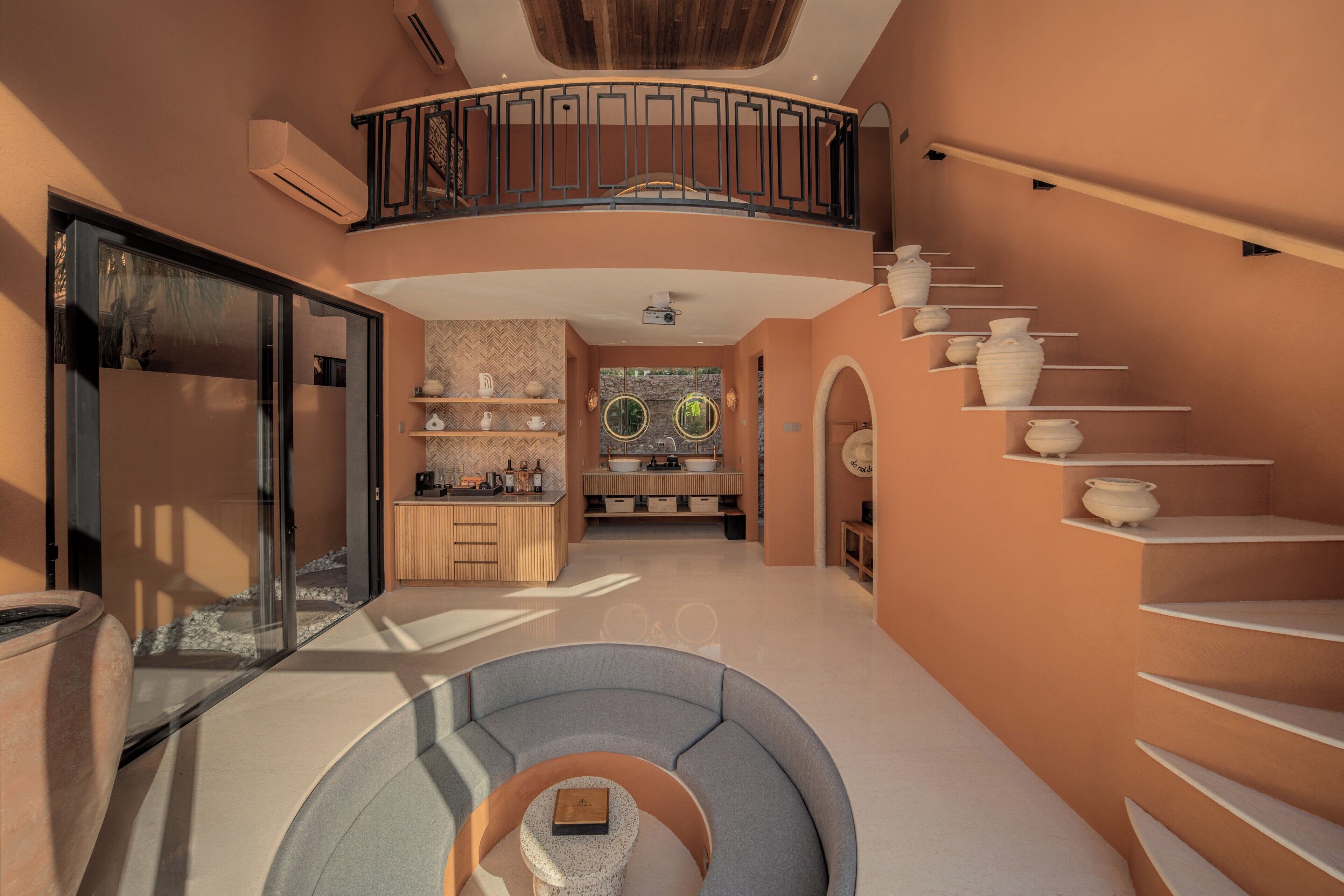 A spacious interior with a curved seating area, a kitchen with a herringbone backsplash, and a staircase with white shelves.