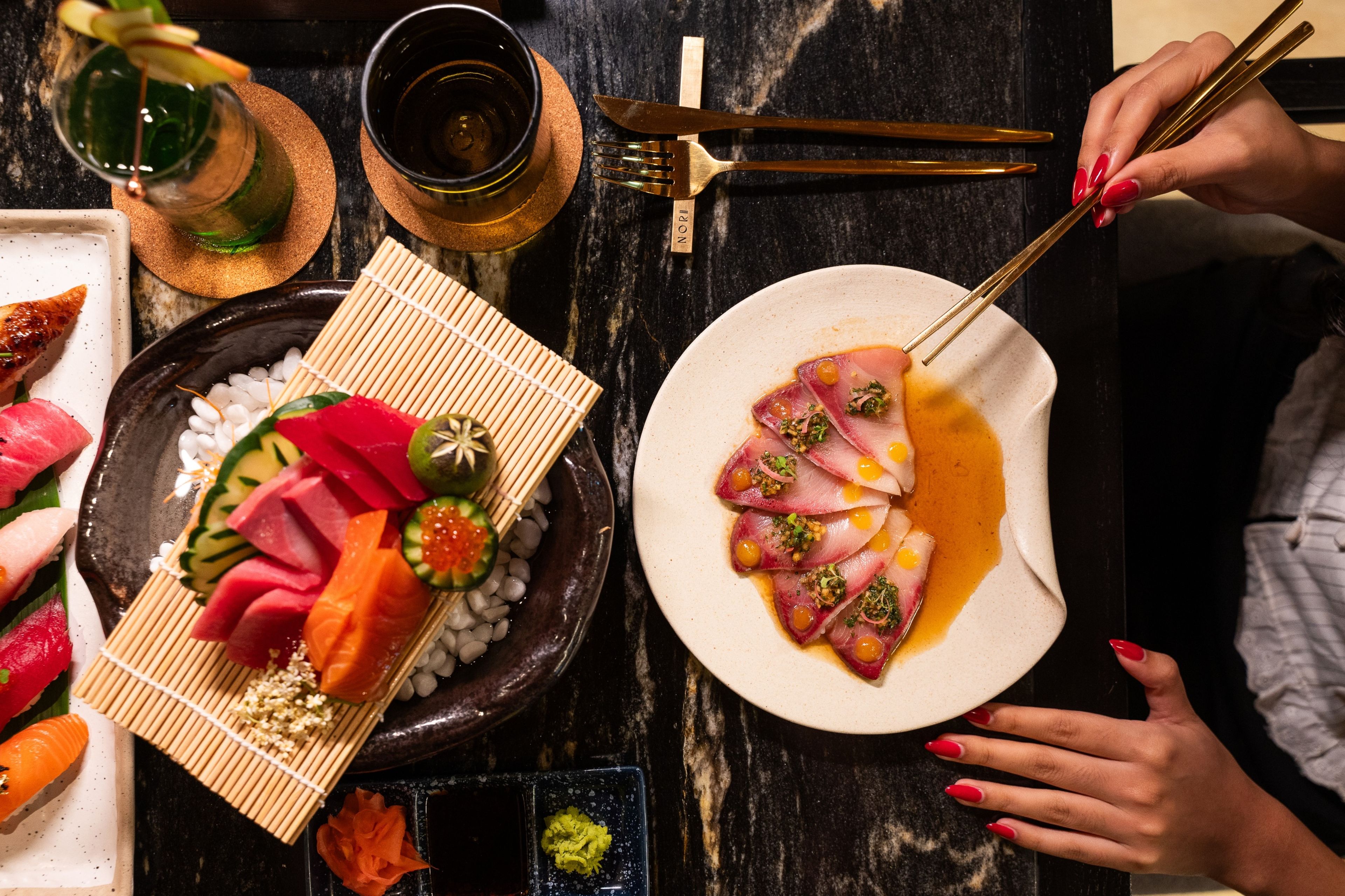 A dining table with various dishes, chopsticks, and a person holding them.