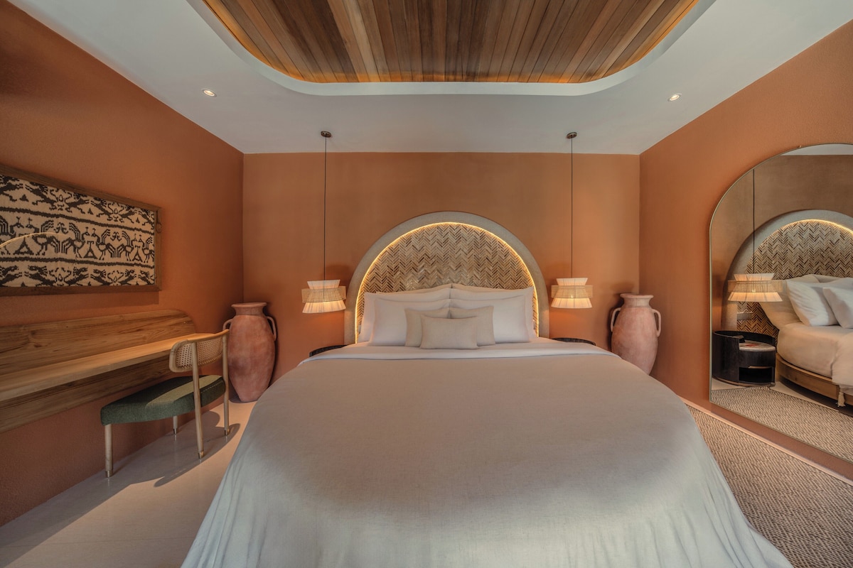 Een slaapkamer met een groot bed, twee bedlampen, een houten bureau en een spiegel.