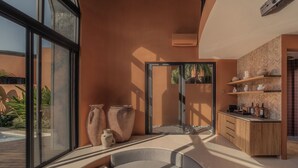 A modern interior with a curved seating area, large windows, and a kitchen with wooden shelves. - Ajowa Resort & Spa Seminyak by Ini Vie Hospitality (Keroboken Kelod)