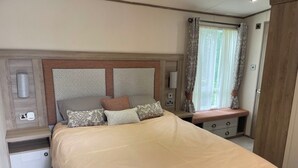 Una cama bien hecha con cabecera, mesitas de noche y una ventana con cortinas.