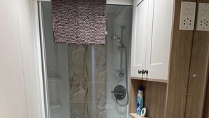 Una ducha con puerta de vidrio, una toalla colgada en la puerta y un armario de madera con un estante abajo.