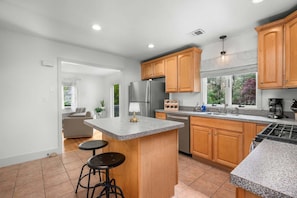 A modern kitchen with granite countertops, wooden cabinets, a stainless steel refrigerator, and a built-in oven. - Cape Cod Home Near 3 Beaches (Cotuit)