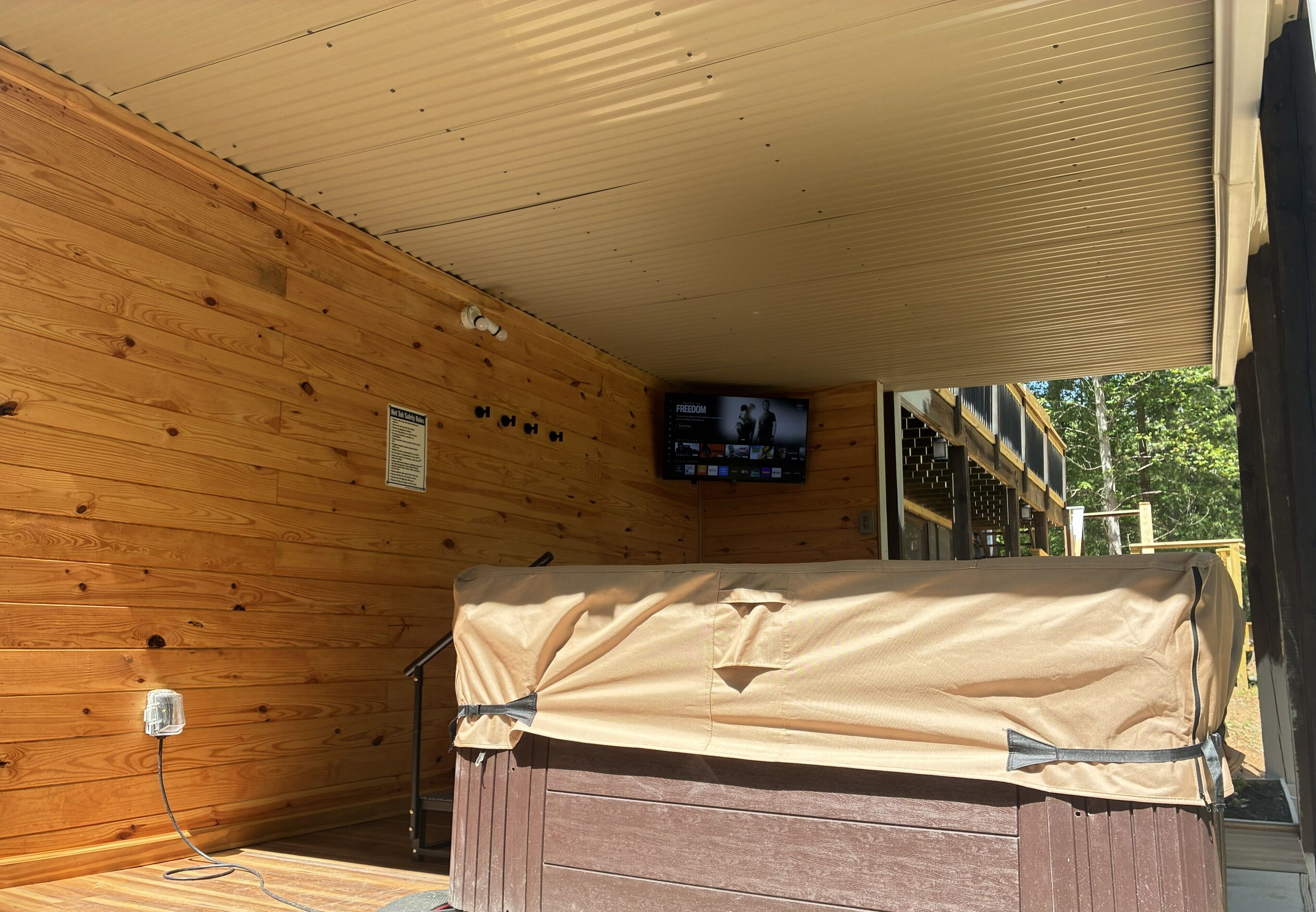 Una cabaña de madera con un televisor montado en la pared, un banco cubierto y un ventanal con vistas a una terraza.