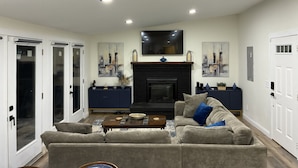 A living room with a sofa, coffee table, fireplace, TV, and artwork on the walls. - Lake House Retreat with Lakeside Hot Tub (Roxboro)