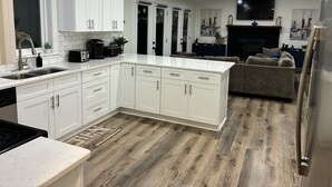 A modern kitchen with white cabinetry, a central island, and a dining area with a sofa. - Lake House Retreat with Lakeside Hot Tub (Roxboro)