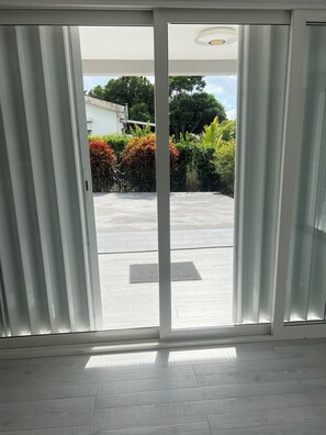 Ein Zimmer mit einer Schiebetür und Zugang zu einem Außenbereich mit befestigtem Untergrund und Grünflächen.