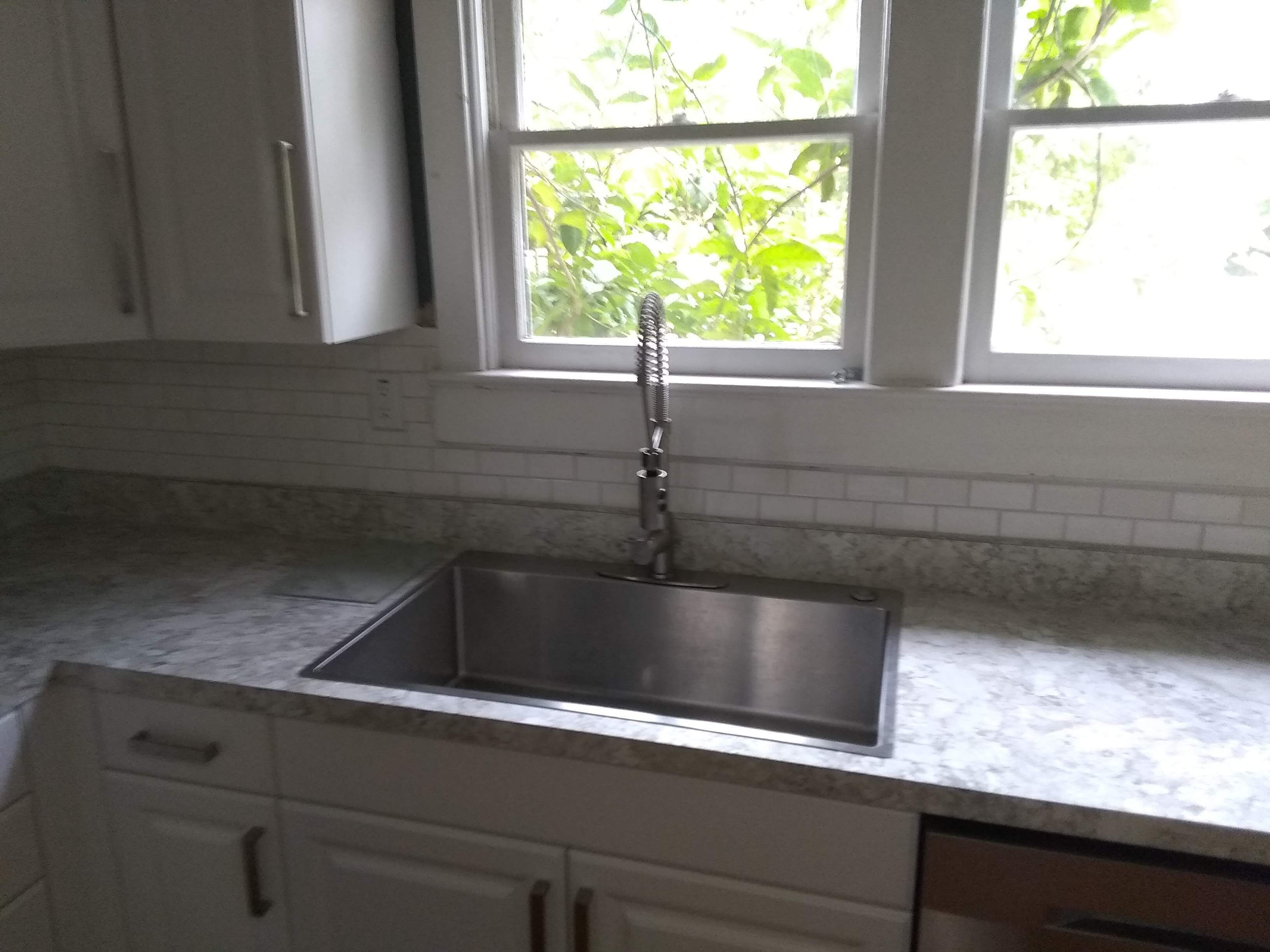 A kitchen with a stainless steel sink, white cabinets, and a window with a view of greenery.