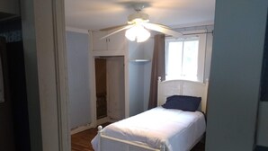 Een slaapkamer met een bed, een plafondventilator, een raam en een deur.