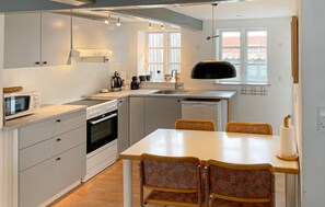 A compact kitchen with a microwave, stove, sink, and a dining area with chairs. - Cozy home in Rudkøbing with WiFi (Rudkøbing)