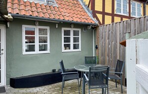 A house with a tiled roof, two windows, a table with chairs, and a wooden fence. - Cozy home in Rudkøbing with WiFi (Rudkøbing)