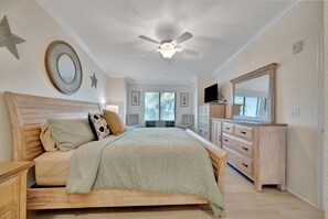 Een slaapkamer met een bed, een houten hoofdbord, nachtkastjes, een dressoir, een plafondventilator en een grote spiegel.