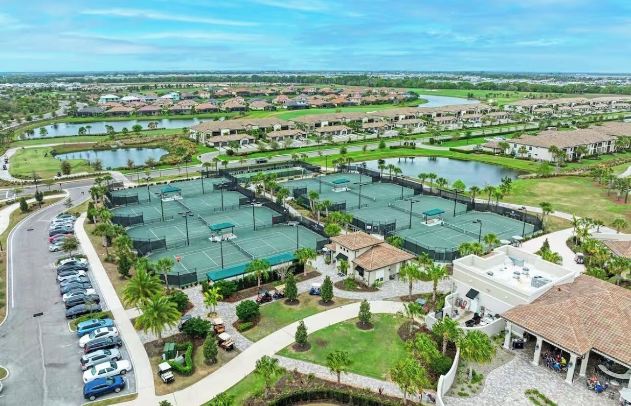 Zona residencial con varias canchas de tenis, un estacionamiento y una masa de agua.