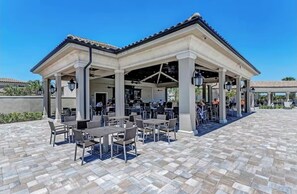 Eine Terrasse im Freien mit Tischen und Stühlen, ein überdachter Sitzbereich und ein klarer, blauer Himmel.