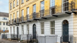 A multi-story building with a white facade, black railings, and a street in front. - Stunning Flat in Centre of Cheltenham (Cheltenham)