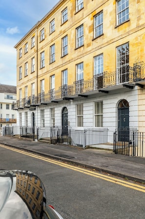 A multi-story building with a white facade, black railings, and a street in front. - Stunning Flat in Centre of Cheltenham (Cheltenham)