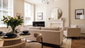 A living room with a sofa, chairs, a TV, a fireplace, and a chandelier. - Stunning Flat in Centre of Cheltenham (Cheltenham)