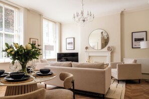 A living room with a sofa, chairs, a TV, a fireplace, and a chandelier. - Stunning Flat in Centre of Cheltenham (Cheltenham)