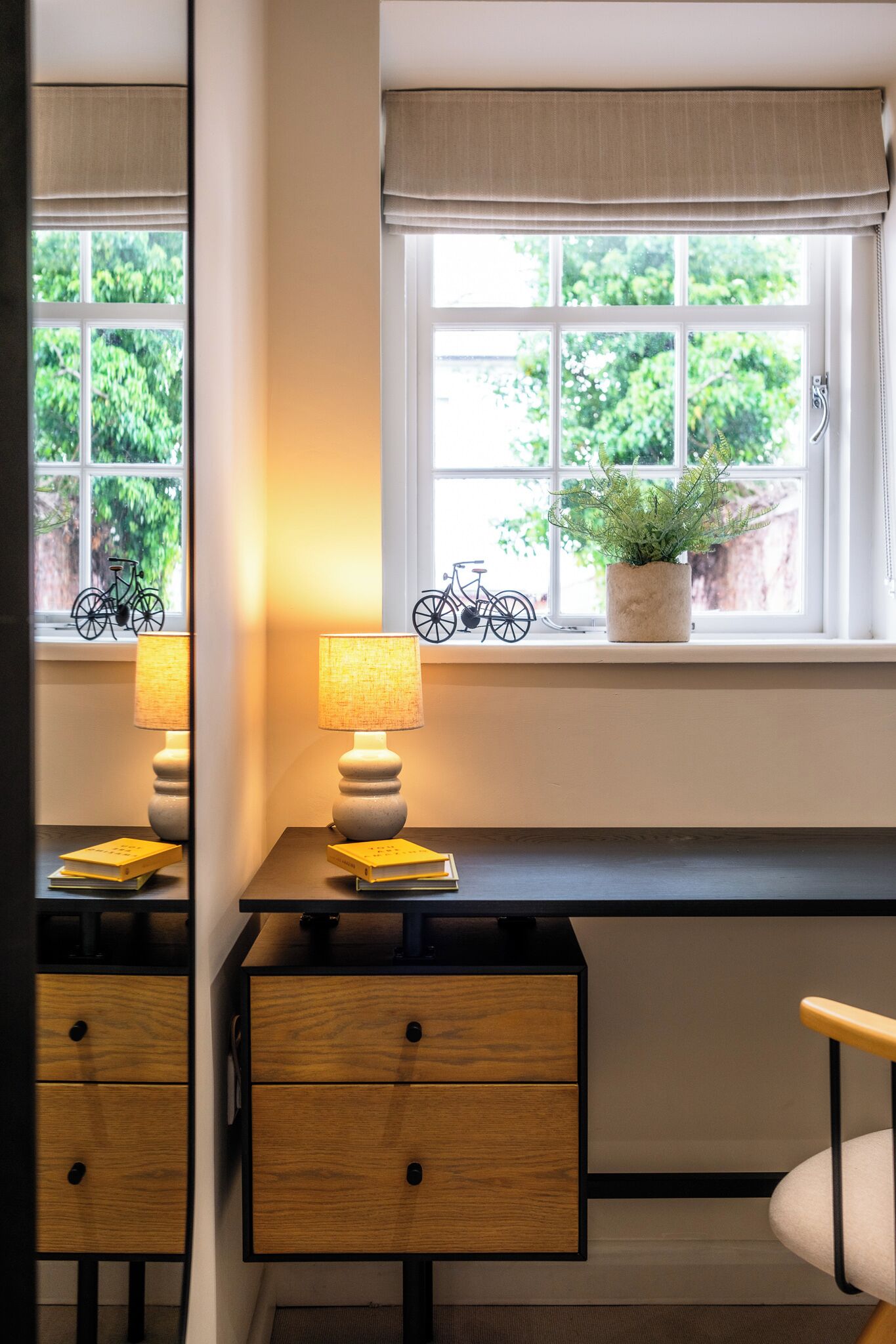 A room with a desk, a lamp, a window with a plant, and a bicycle decoration.