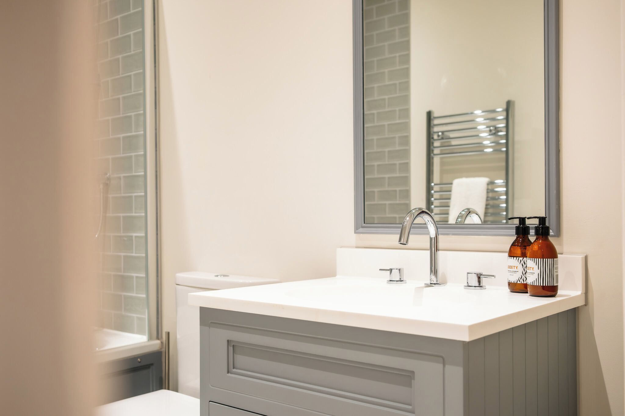 A bathroom with a white sink, a mirror, a towel rack, and two bottles on the counter.