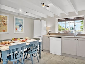 A modern kitchen with white cabinetry, a dining table with blue chairs, and a window with a view of greenery.