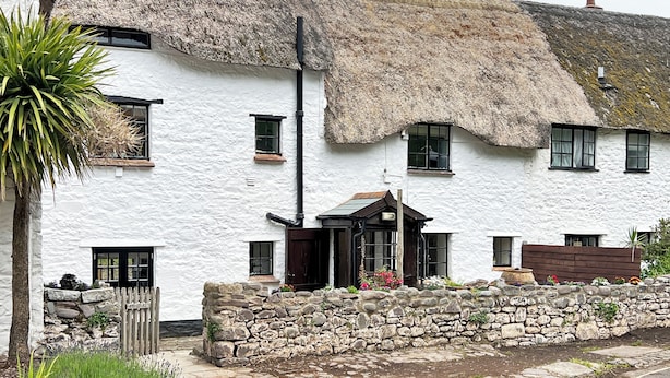 A white building with a thatched roof, stone wall, and a wooden gate. - Bobs Cottage, Porlock Weir (Porlock Weir)