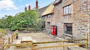 A stone building with a thatched roof, wooden benches, and a gravel courtyard. - Bobs Cottage, Porlock Weir (Porlock Weir)