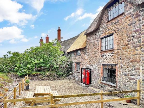 A stone building with a thatched roof, wooden benches, and a gravel courtyard.