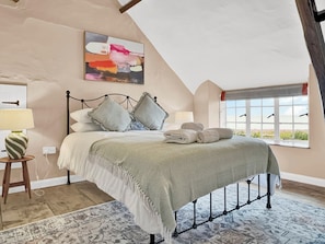 A bedroom with a bed, pillows, a bedside lamp, a rug, a painting, and a window with a view.