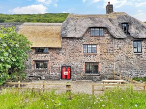A stone building with a thatched roof, a red mailbox, and a wooden fence.