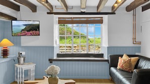 A room with a wooden ceiling, a window with a view of greenery, a black leather sofa, and a small white table with a lamp. - Bobs Cottage, Porlock Weir (Porlock Weir)