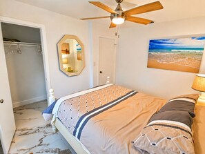 A bedroom with a bed, a ceiling fan, a mirror, a door, and a beach painting. - Beautiful remodeled House in Nice area 5 min from downtown. (Fort Myers)