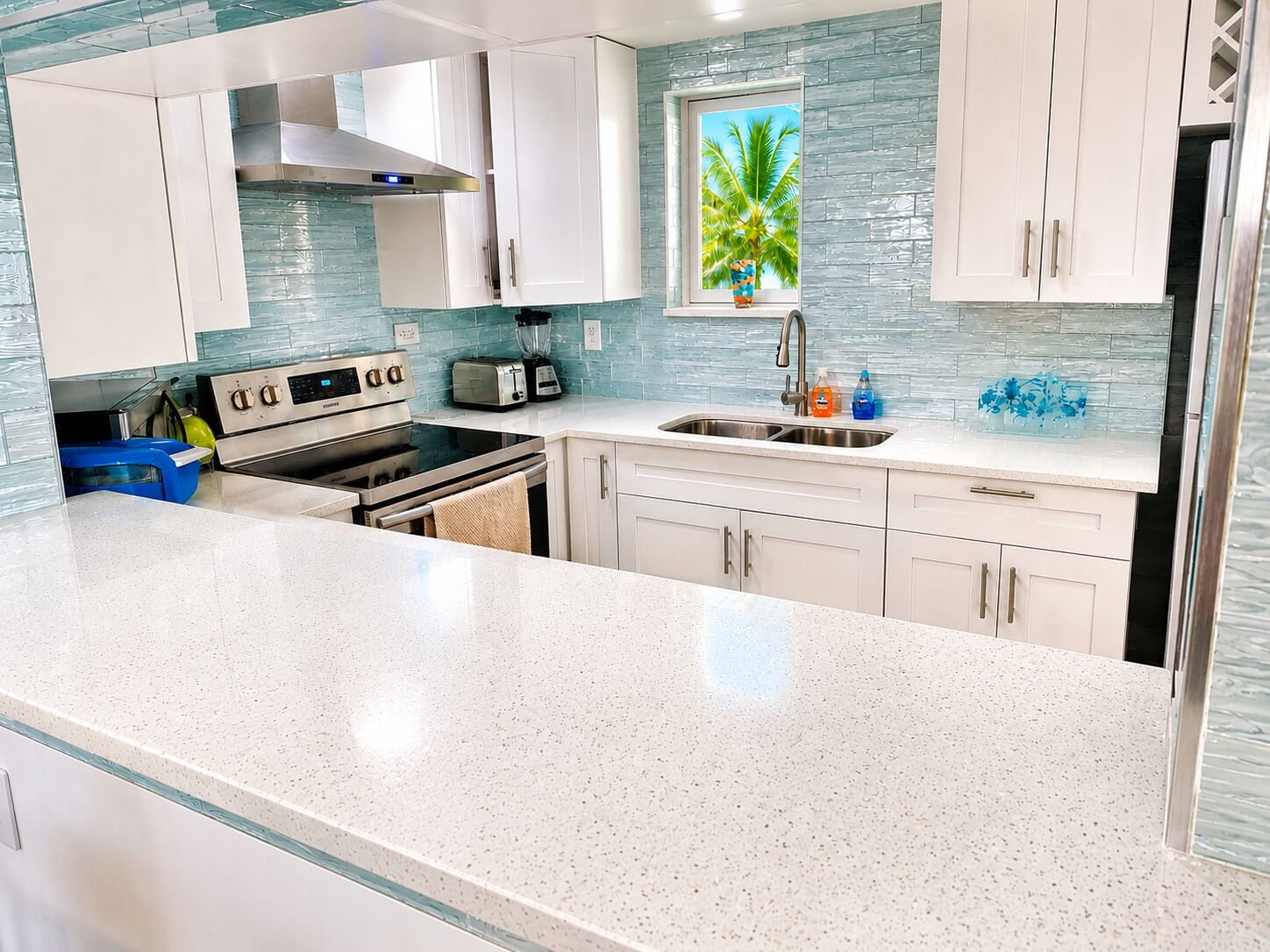 A modern kitchen with white cabinetry, a stainless steel range, and a window with a tropical view.