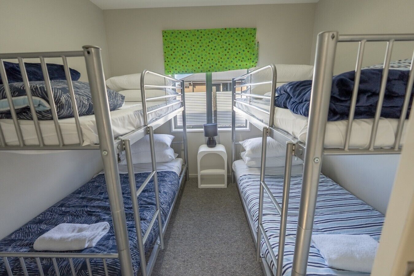 Ein Schlafsaalzimmer mit Etagenbetten, einem kleinen Hocker und einem grün gemusterten Vorhang.