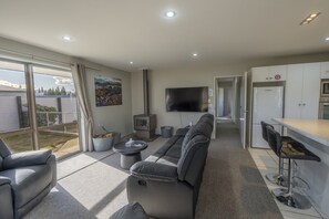 A modern living room with a sofa, a TV, a fireplace, and a kitchen area with a fridge and bar stools.