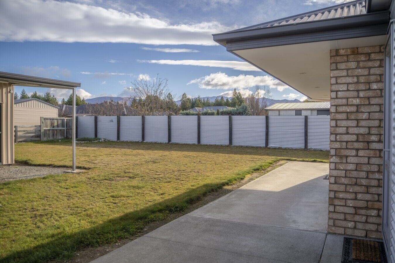A residential backyard with a concrete patio, a brick wall, and a metal fence.
