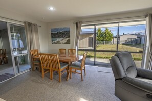 A dining area with a table and chairs, a sofa, and a large window with a view of a rural landscape.