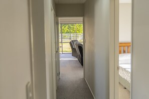 A narrow hallway leading to a balcony with a view of trees and a fence.